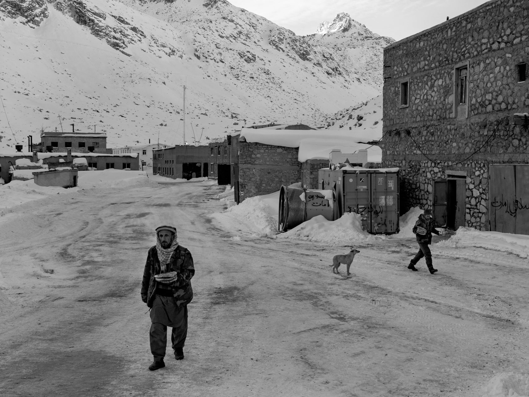 Workers at the maintenance village in Northern Salang, pass through the iced former Soviet base on 3600m altitude as they pick up their room's daily ration for breakfast. The village's stray dog called Max watches them passing by.