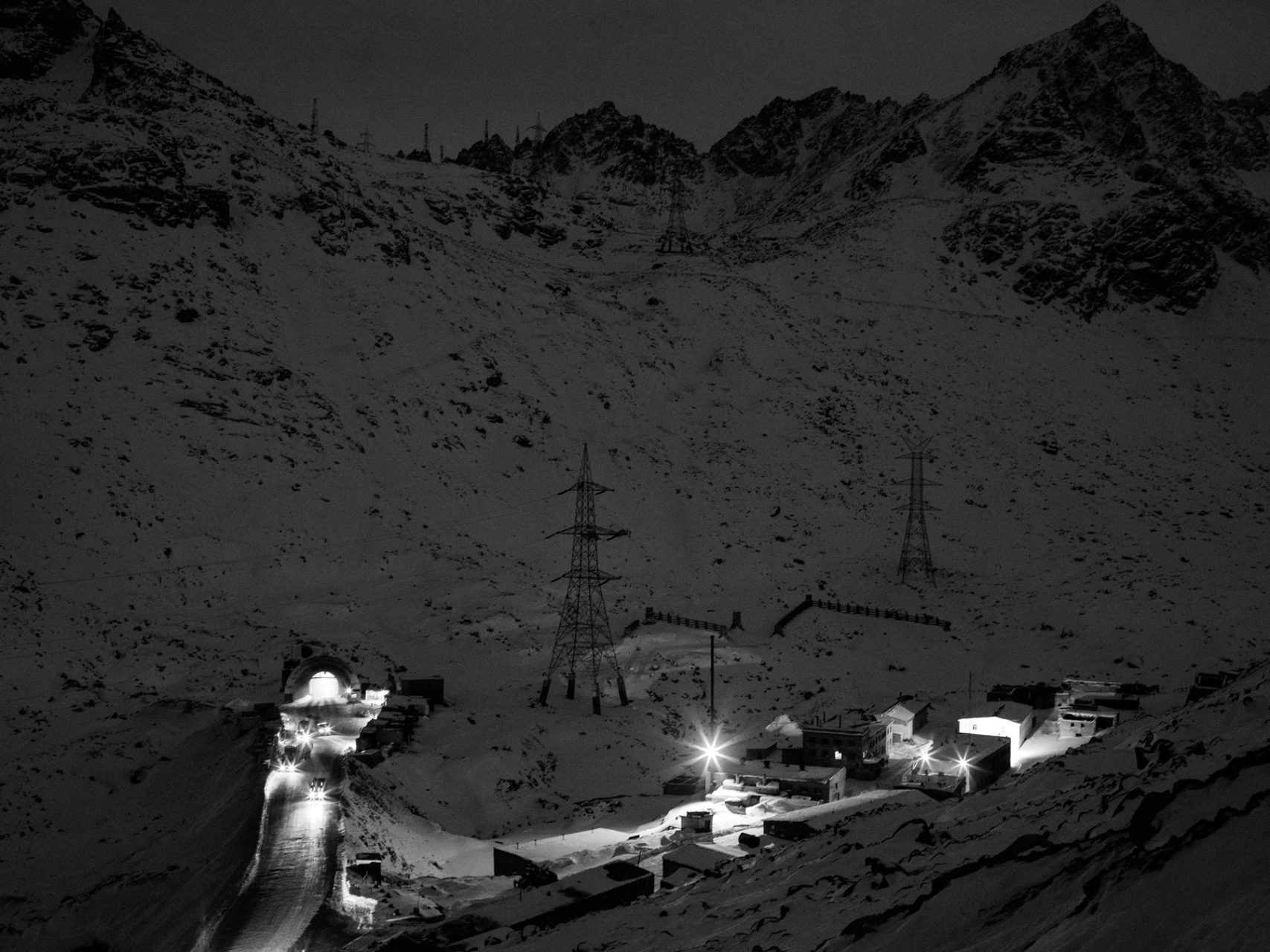 Trucks leave the Northern end of the Salang Tunnel passing the servicing village at 3600m altitude as the dusk sets in.