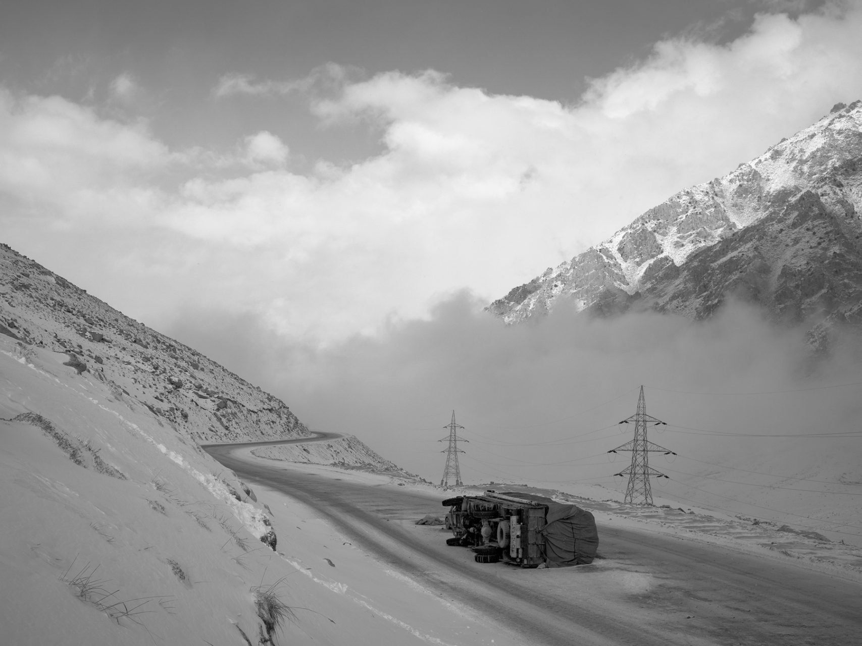 A canted over truck lies on the road of the Northern side of the Salang pass. It needs to be offloaded thus it can be lifted by a crane later.